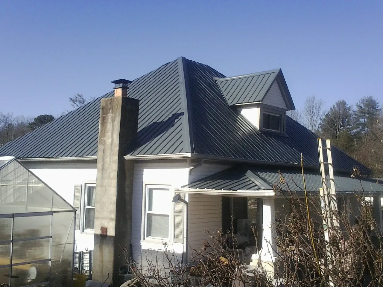 Dark blue standing seam metal roof on a white farmhouse with dormer — Slate & Tile Roof Repair by Roofing Brothers in Carville
