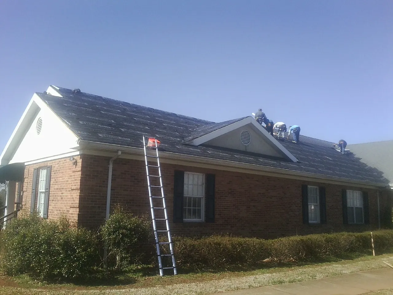 Crew tearing shingles off a brick ranch roof with a ladder set — Metal Roof Repair work by our crew in Carville