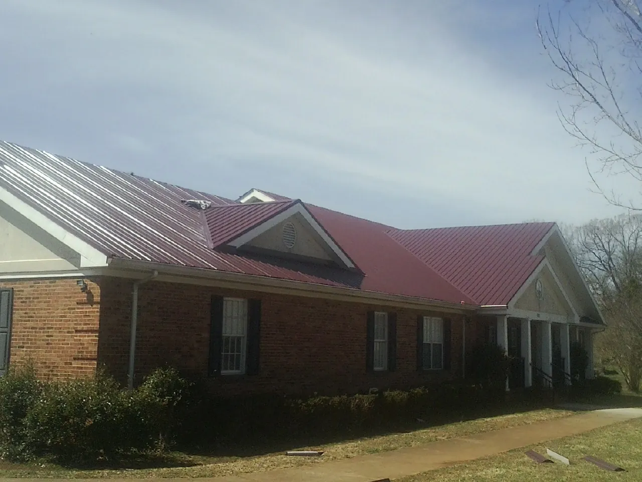 Red metal roof with gabled entries on a long brick building, from a Hail Damage Roof Repair job in Carville