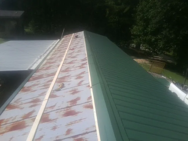 Old rusted panels beside newly installed green metal roofing — Wind Damage Roof Repair by Roofing Brothers in Carville