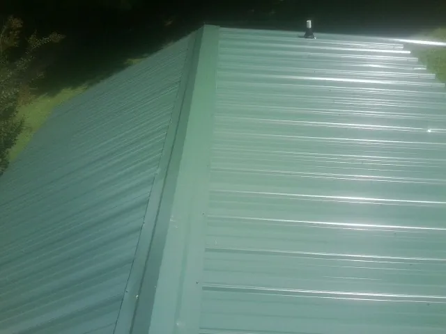 New green metal panels meeting at the ridge of a roof — Flat Roof Repair work by our crew in Carville
