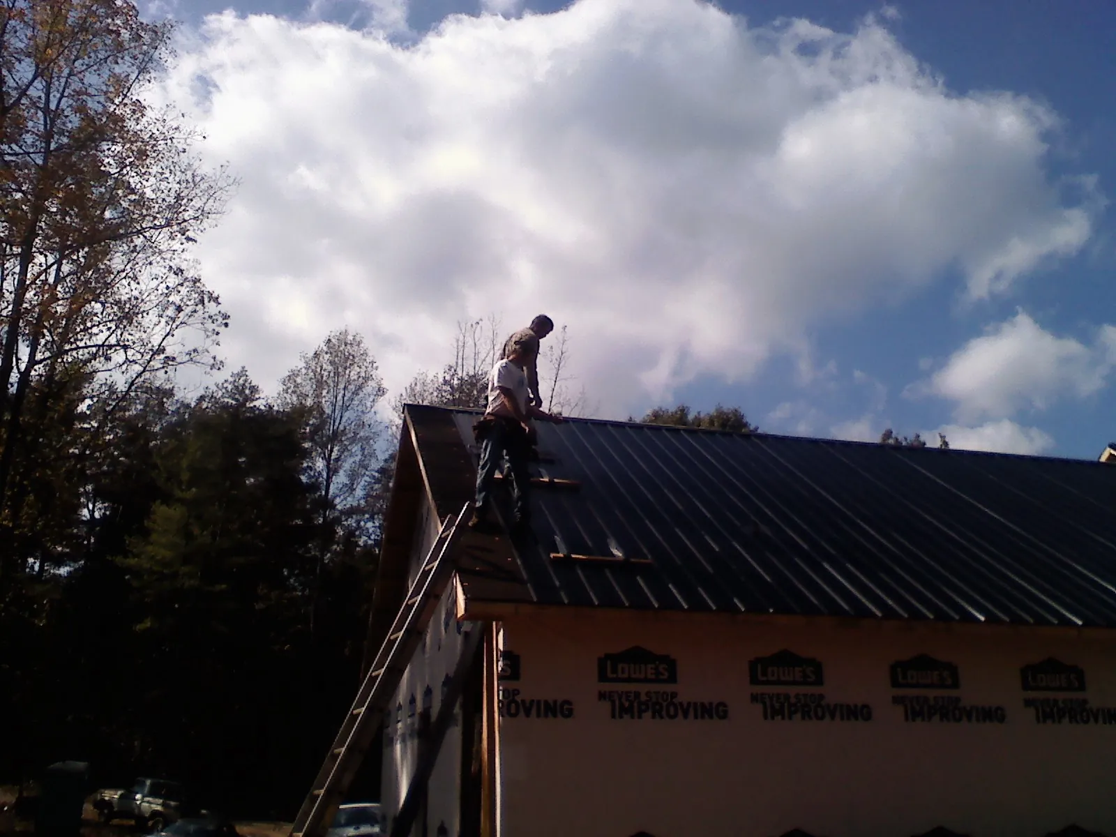Roofer fastening dark metal panels high against a cloudy sky, from a Roof Inspection job in Carville