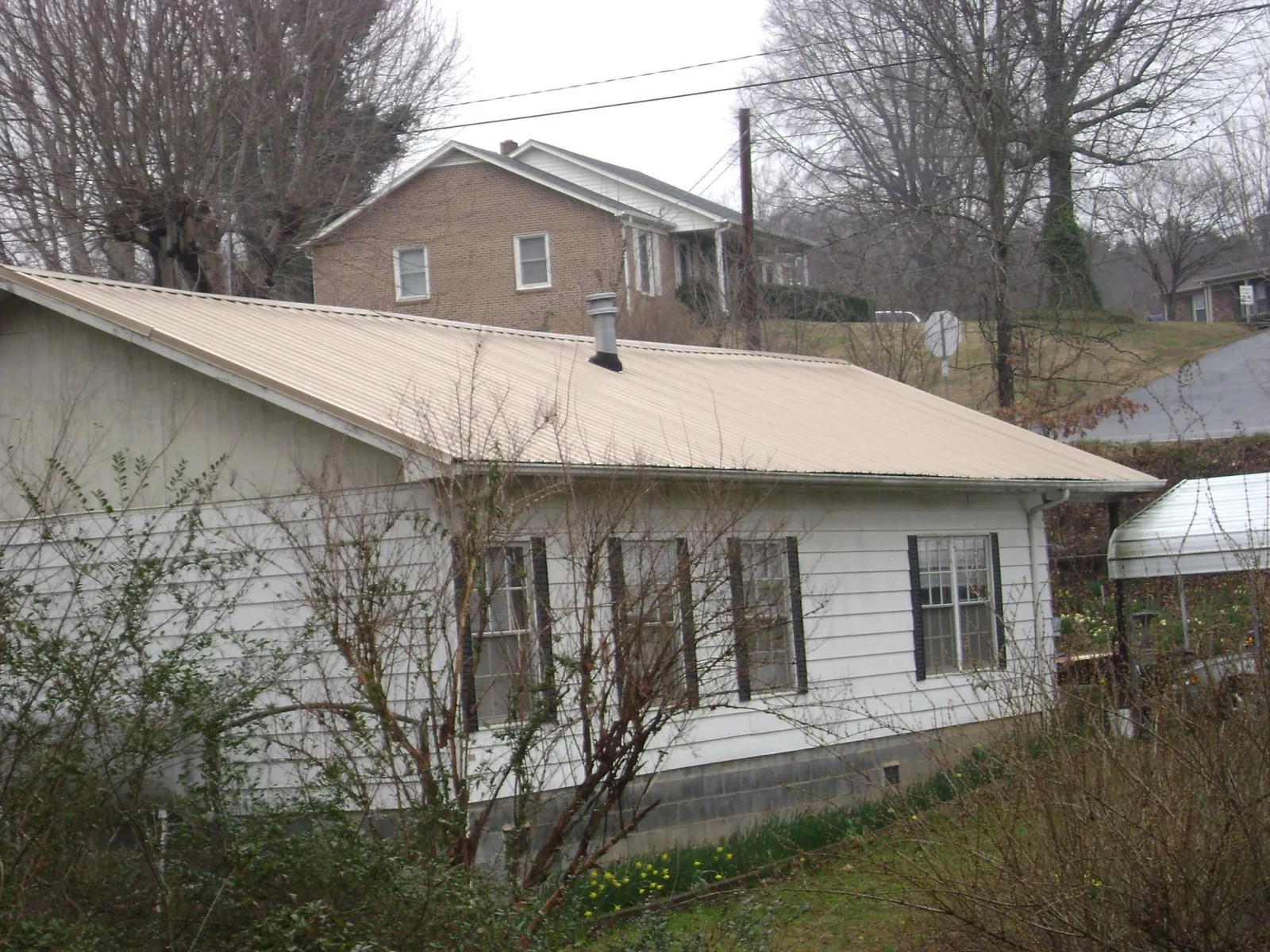 Tan metal roof on a white sided house set into a hillside — Commercial Roofing by Roofing Brothers in Carville