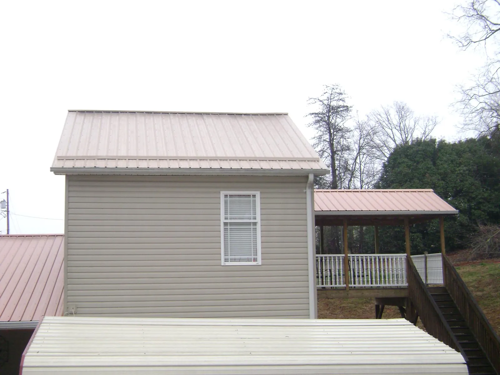 Tan metal roofs on a two story addition and attached porch, from a Roof Replacement job in Carville